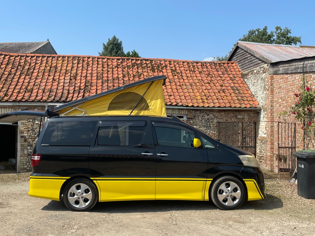 black and yellow Toyota alphard camper van with pop top up sitting in a farmyard
