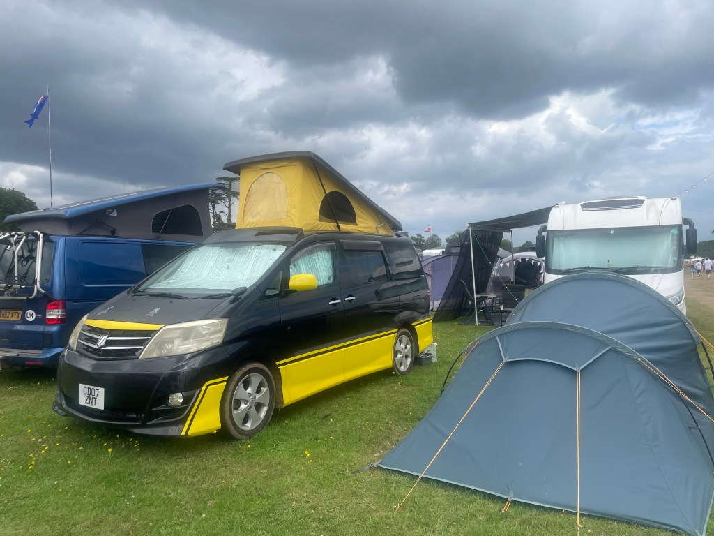 Black and yellow Toyota campervan with a small tent pitched beside it